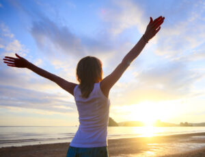 Woman arms outstretched at the beach for a life coaching session for the whole person
